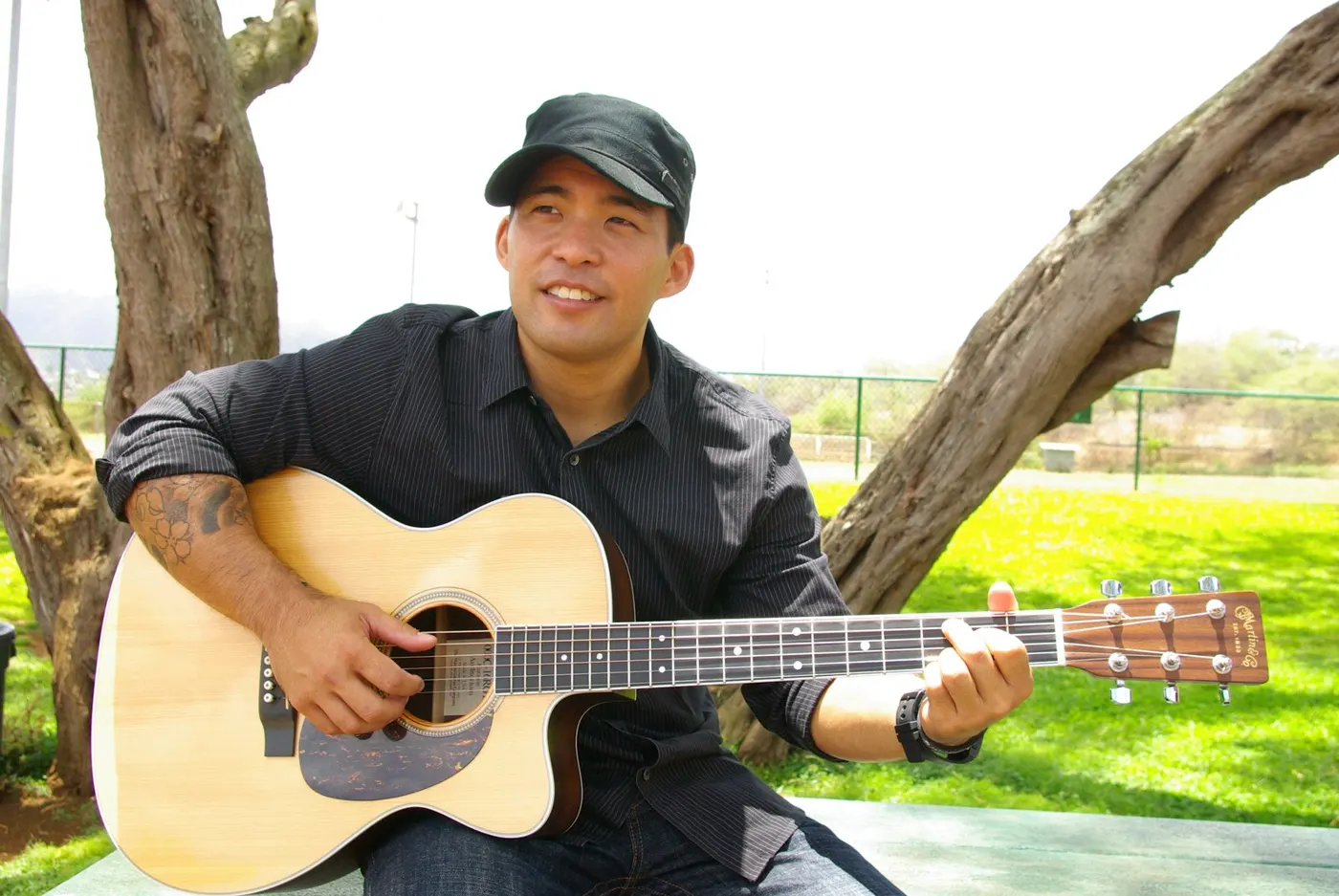 Dayton Watanabe playing guitar under a tree